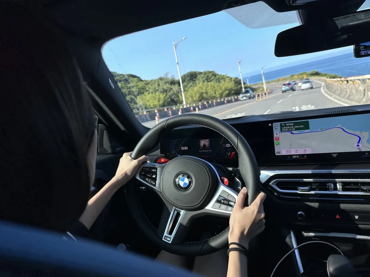 學員握著 BMW 方向盤沿北海岸公路前進，窗外是藍天、海和綠色山丘